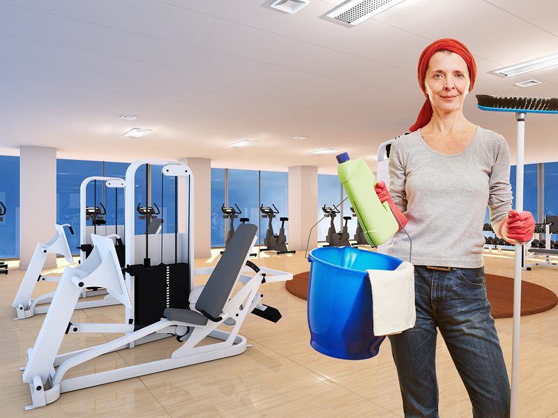 Elderly cleaning lady with cleaning supplies standing in a fitness center